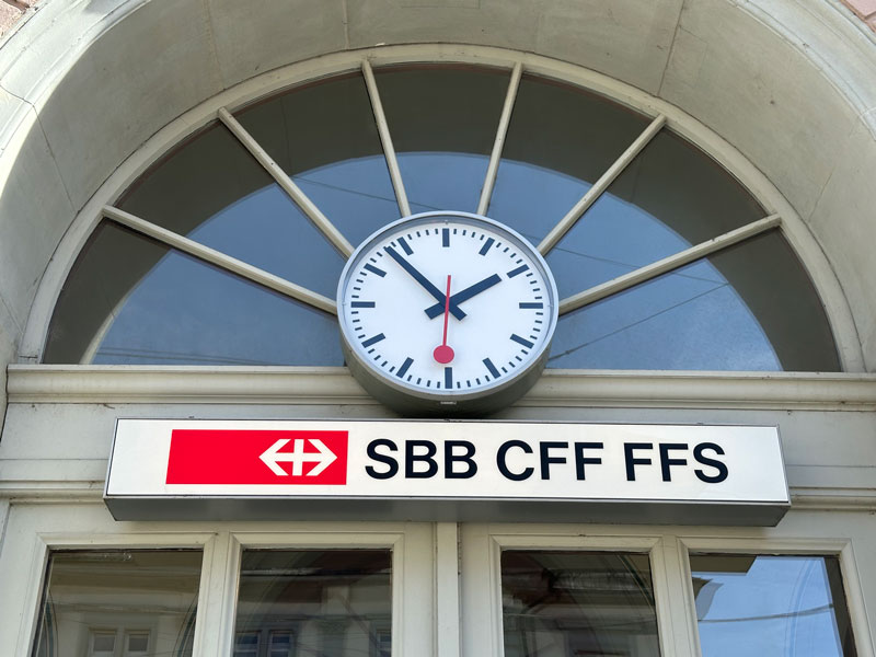 Abbildung einer Schweizer Bahnhofsuhr an einem Bahnhofsgebäude